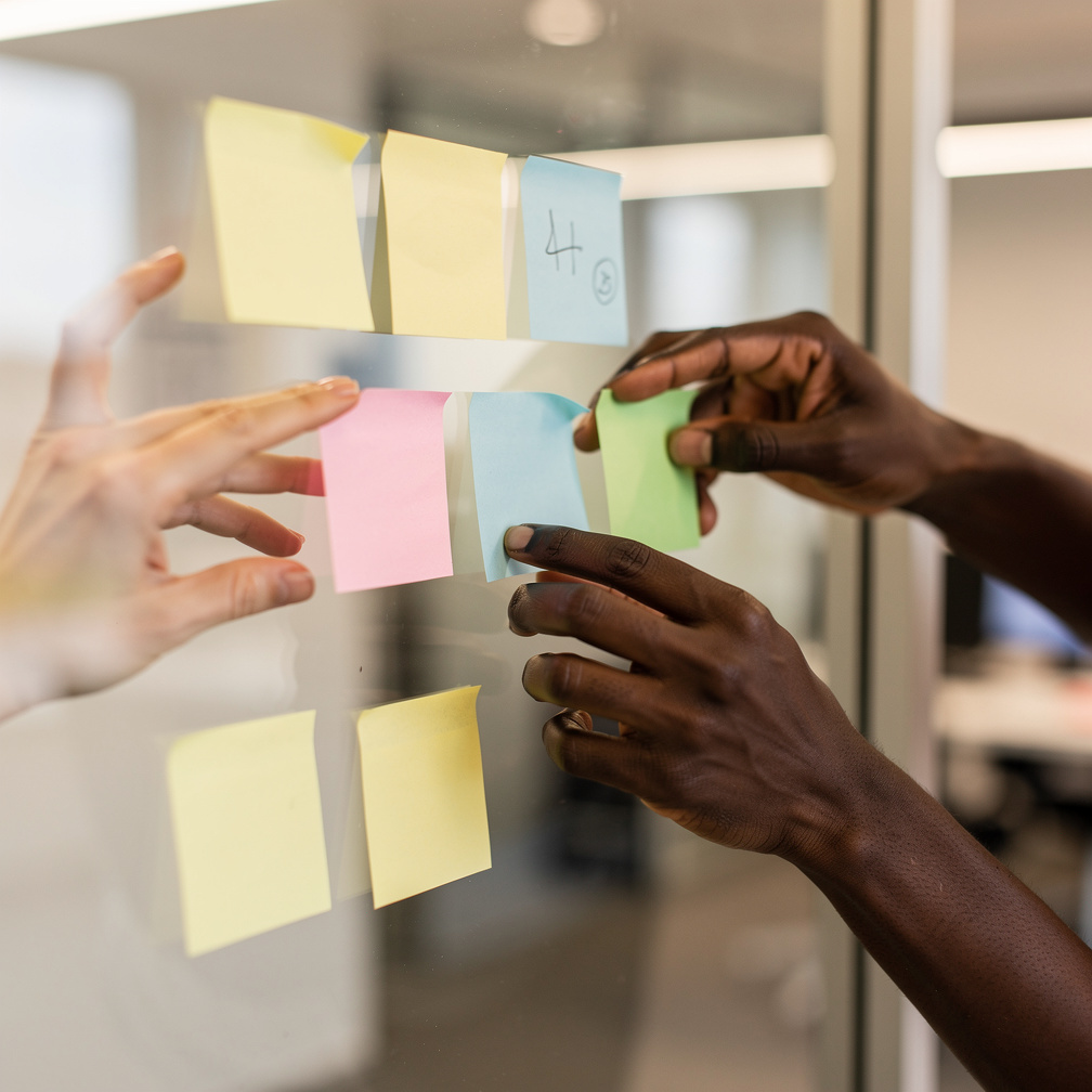 Close-up of hands writing sticky notes together on a whiteboard
